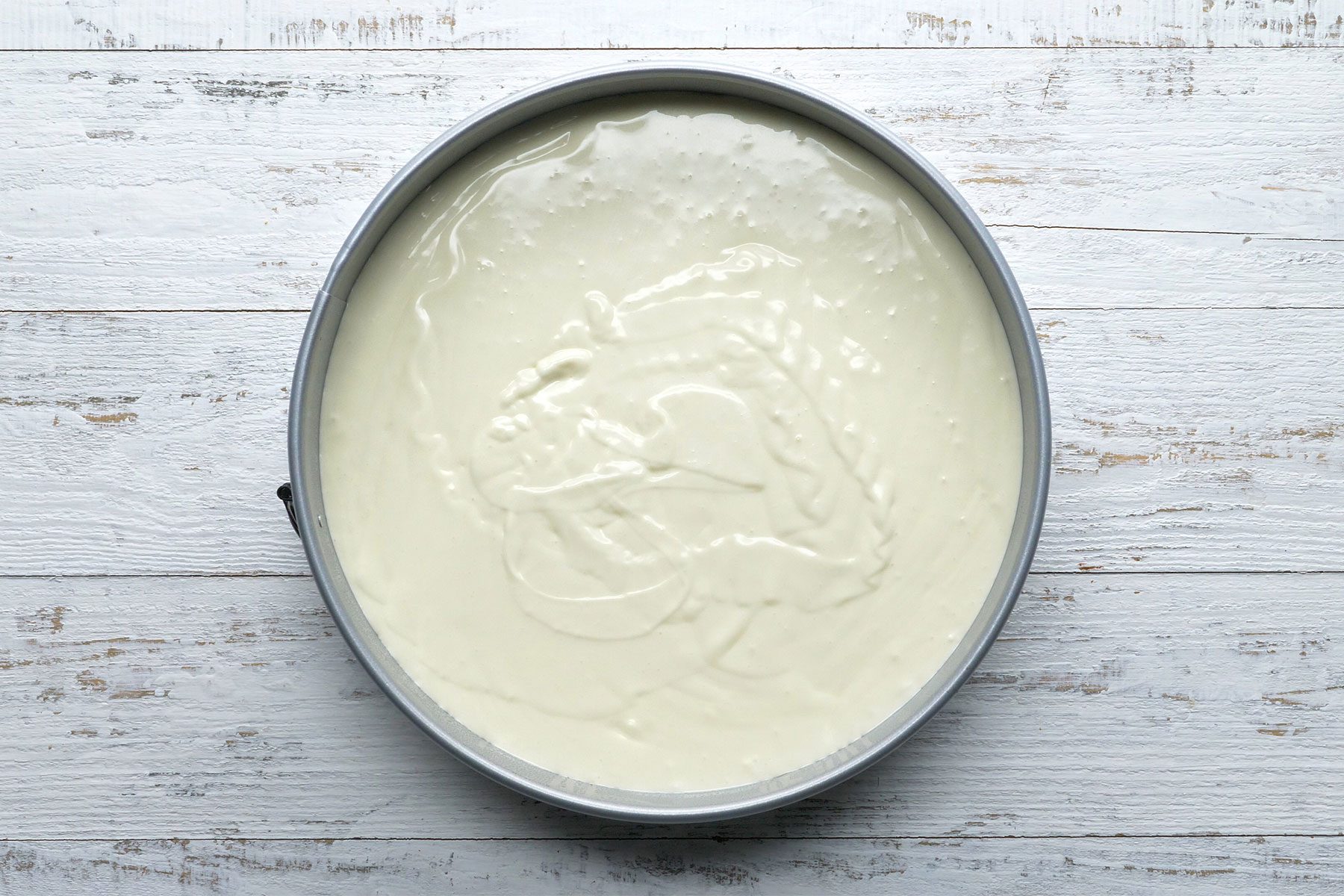 Overhead shot of pan; spread mixture over crust; wooden background;