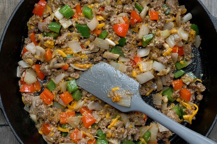 Close shot of remove skillet from heat; added 1/2 cup cheese, ketchup, salt and pepper; mix well; spatula; wooden background;