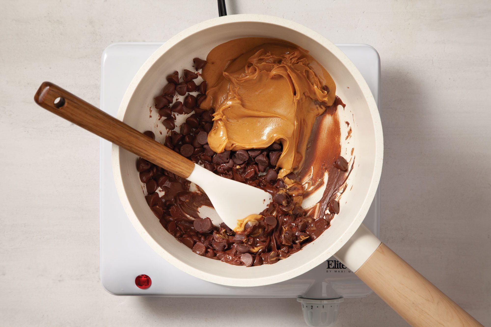 Overhead shot of preparing the frosting; in a small saucepan; combine chocolate chips and peanut butter; cook and stir over low heat until smooth; spatula; induction; marble background;
