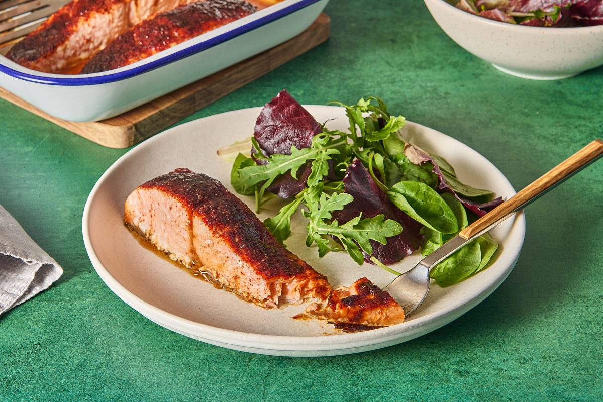 Single piece of baked barbecue salmon on a plate with a salad