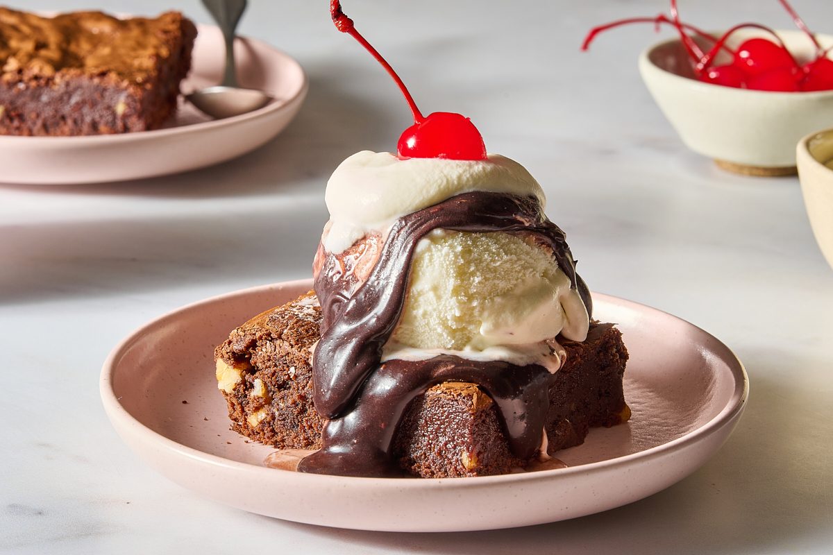 Shot of a chocolate brownie topped with hot fudge sauce, ice cream and a cherry