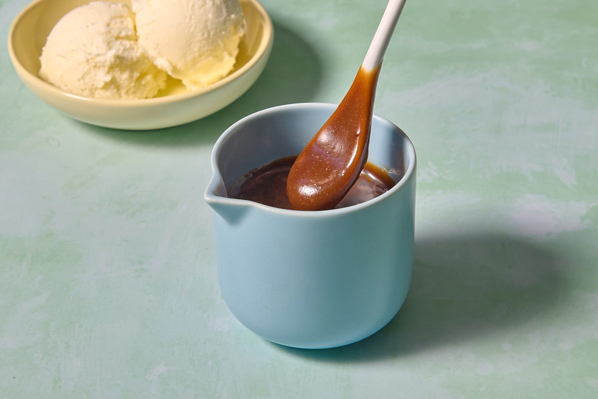 Shot of butterscotch sauce coating a spoon in a small jug