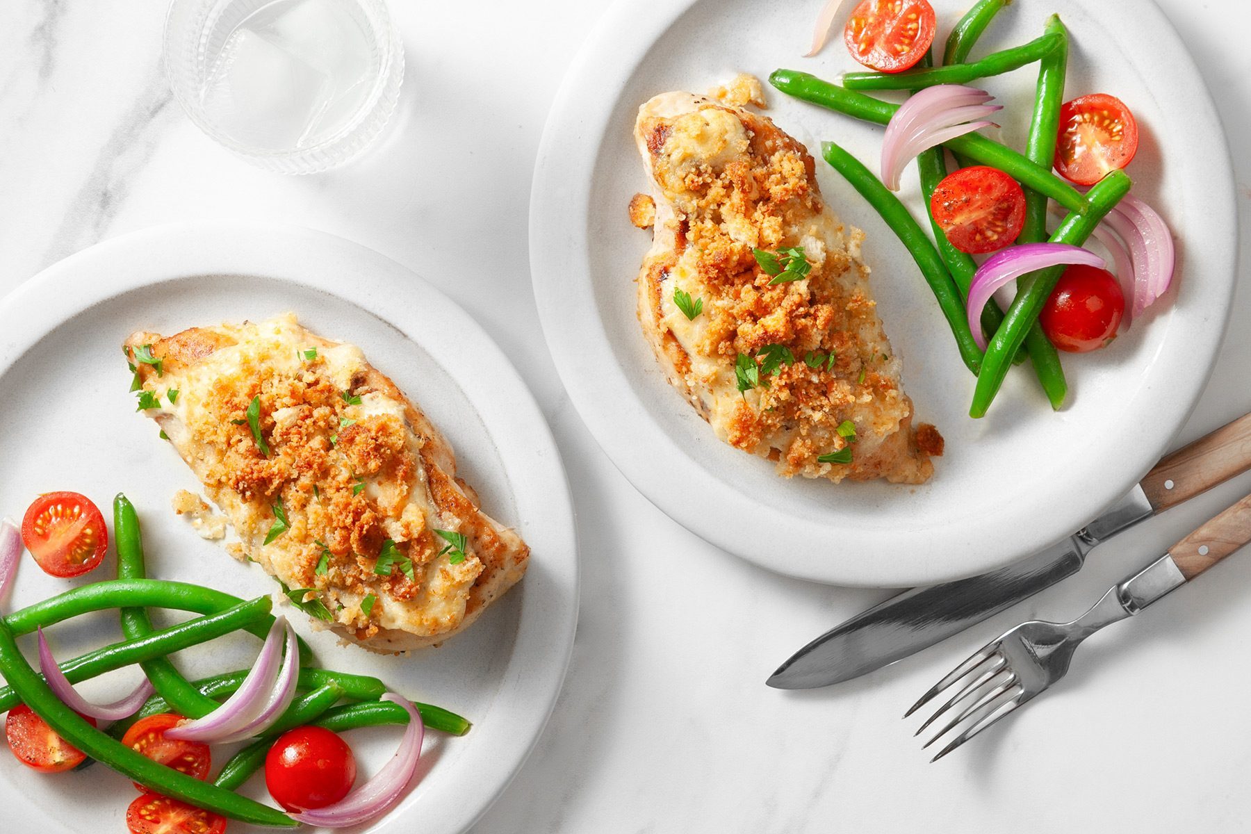 overhead shot; white background; Caesar Chicken served in two white plates with veggies; silver knife and fork