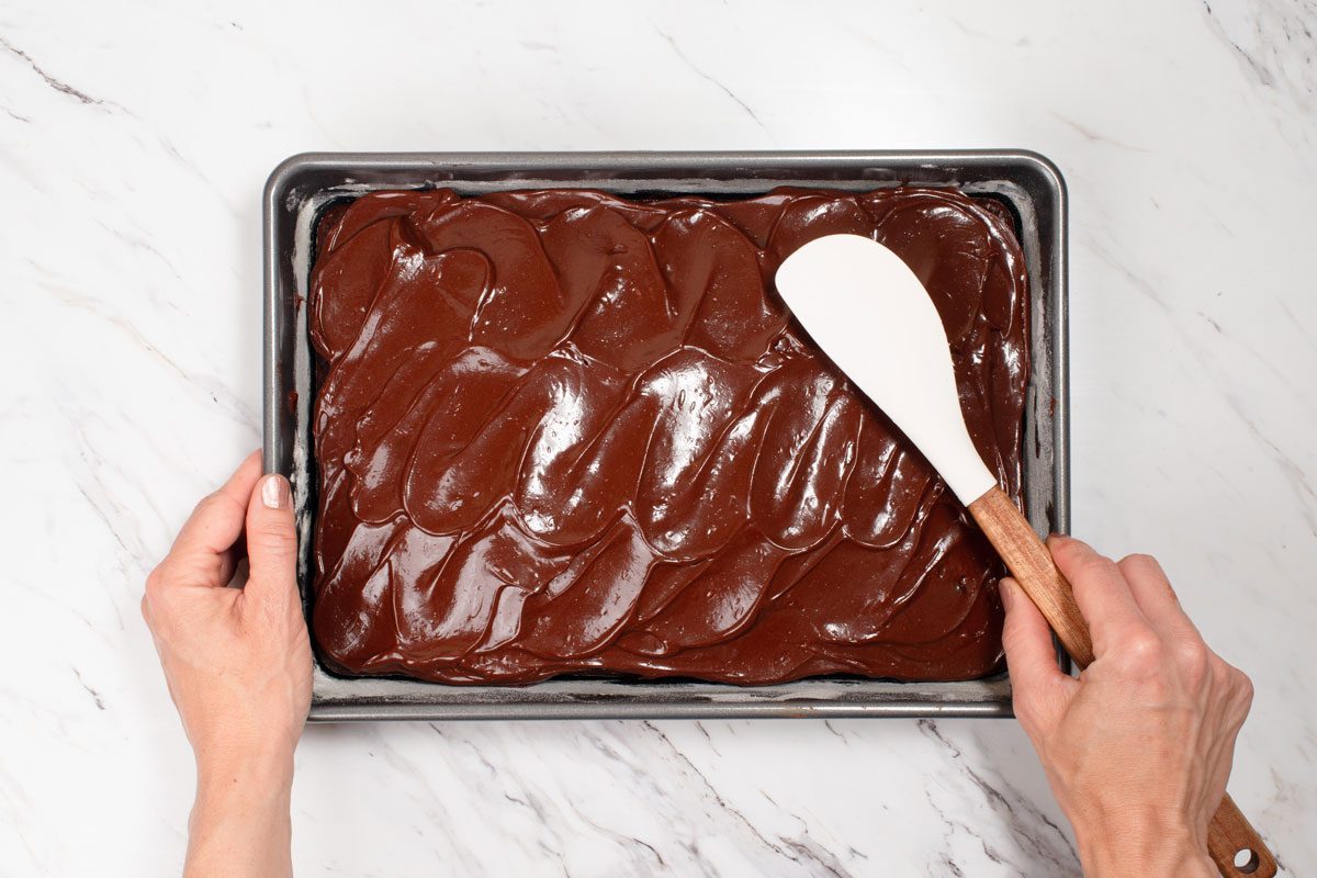 hand spreading the frosting on the Chocolate Zucchini Cake