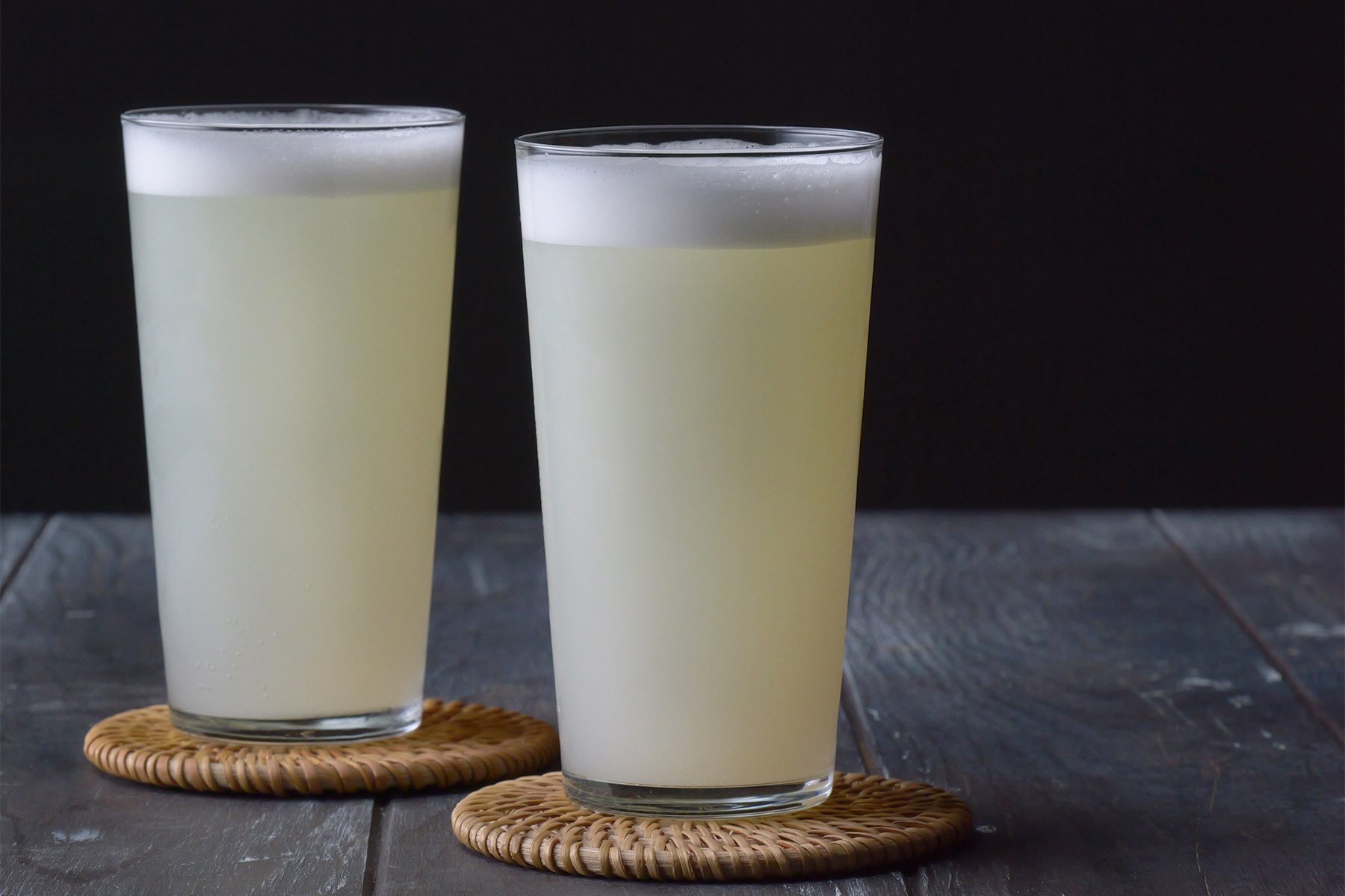 horizontal shot; wooden base; black background; Gin Fizz served in two highball glasses placed over coasters