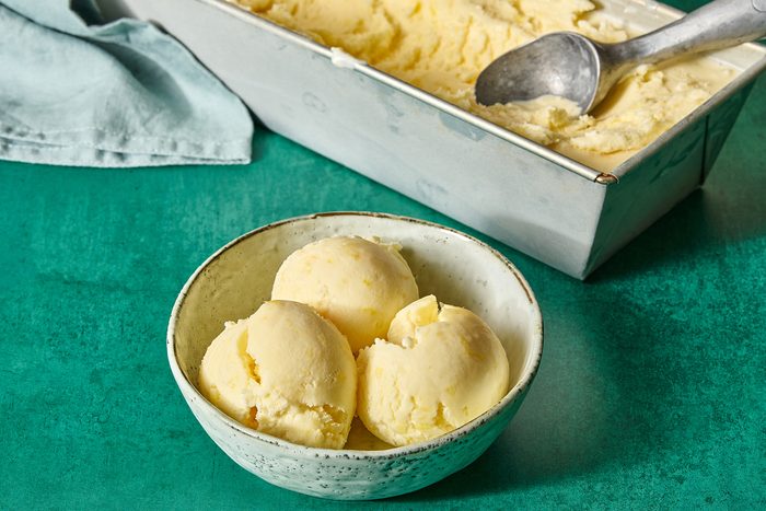 A portion of pineapple ice cream in a bowl with the container in the background