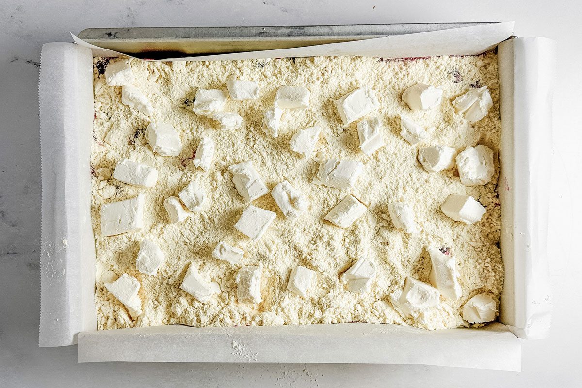 Cubed cream cheese and yellow cake mix in a metal baking pan for Taste of Home Strawberry Cheesecake Dump Cake.