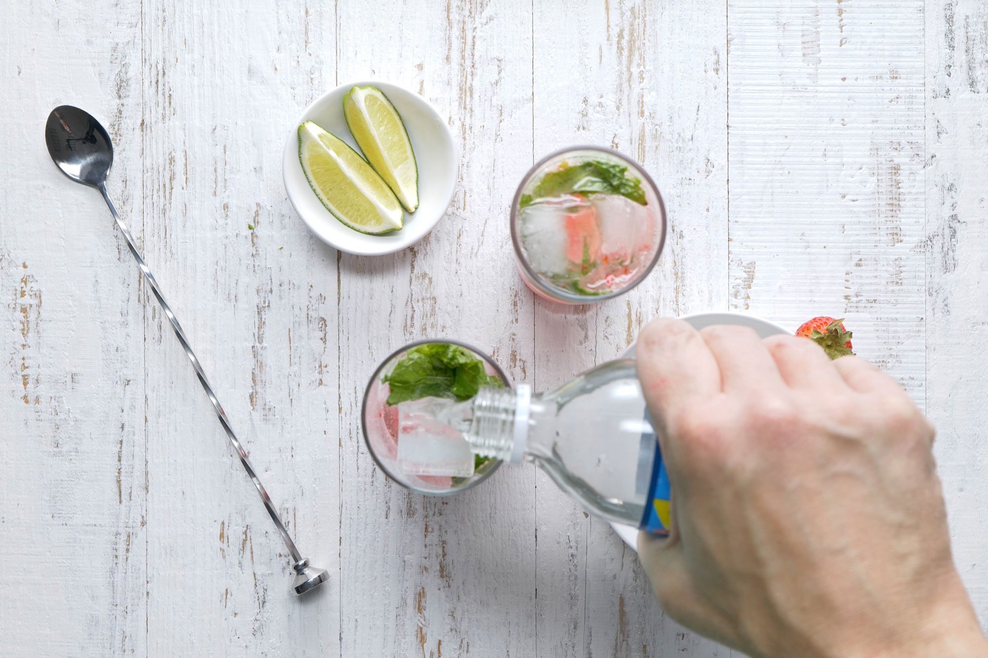 overhead shot; white background; pouring club soda into glass; long sliver spoon;