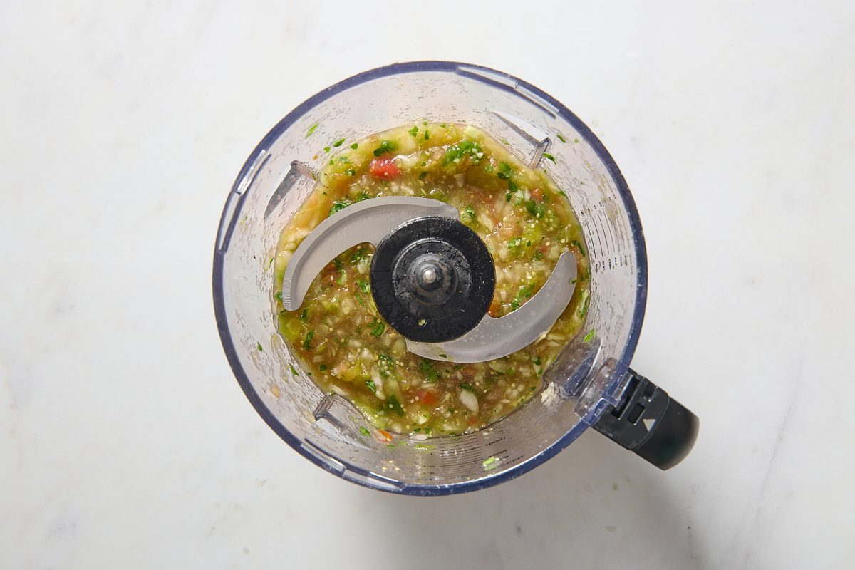 Tomatillo salsa ingredients being blended in a food processor