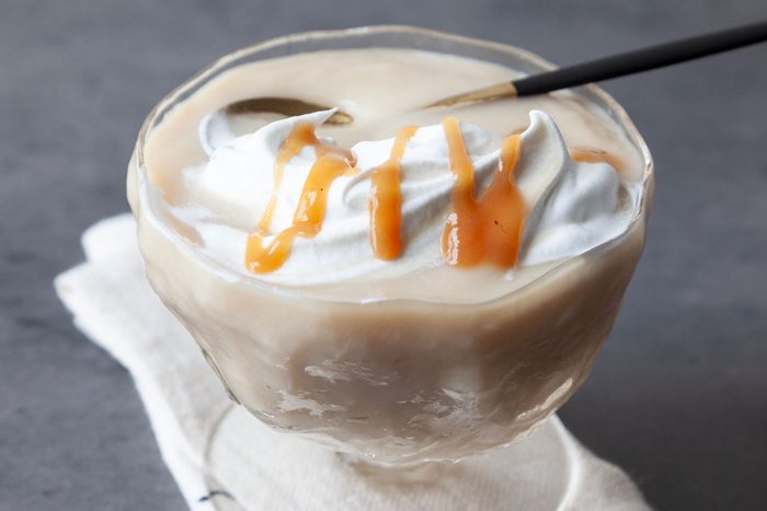 single serving of Taste of Home Caramel Pudding in a glass dessert dish with a small gold and black spoon on a dark gray surface