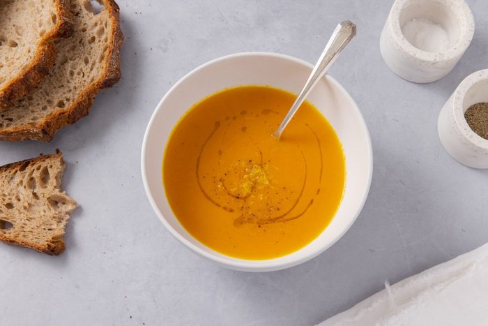 Carrot ginger soup served in bowl with spoon and bread on the side.