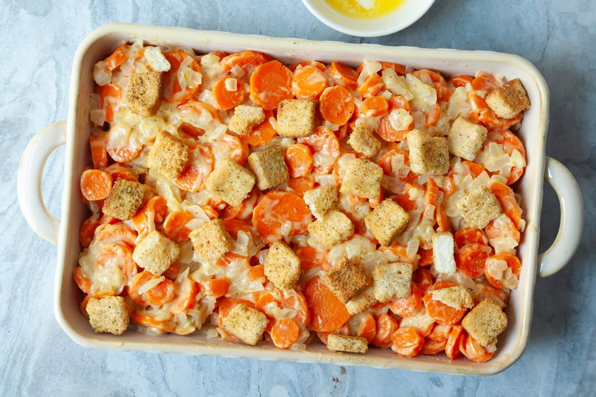 Step 3 of Taste of Home Carrot Casserole is combining the carrots with the onion and soup mixture, then topping with croutons and melted butter