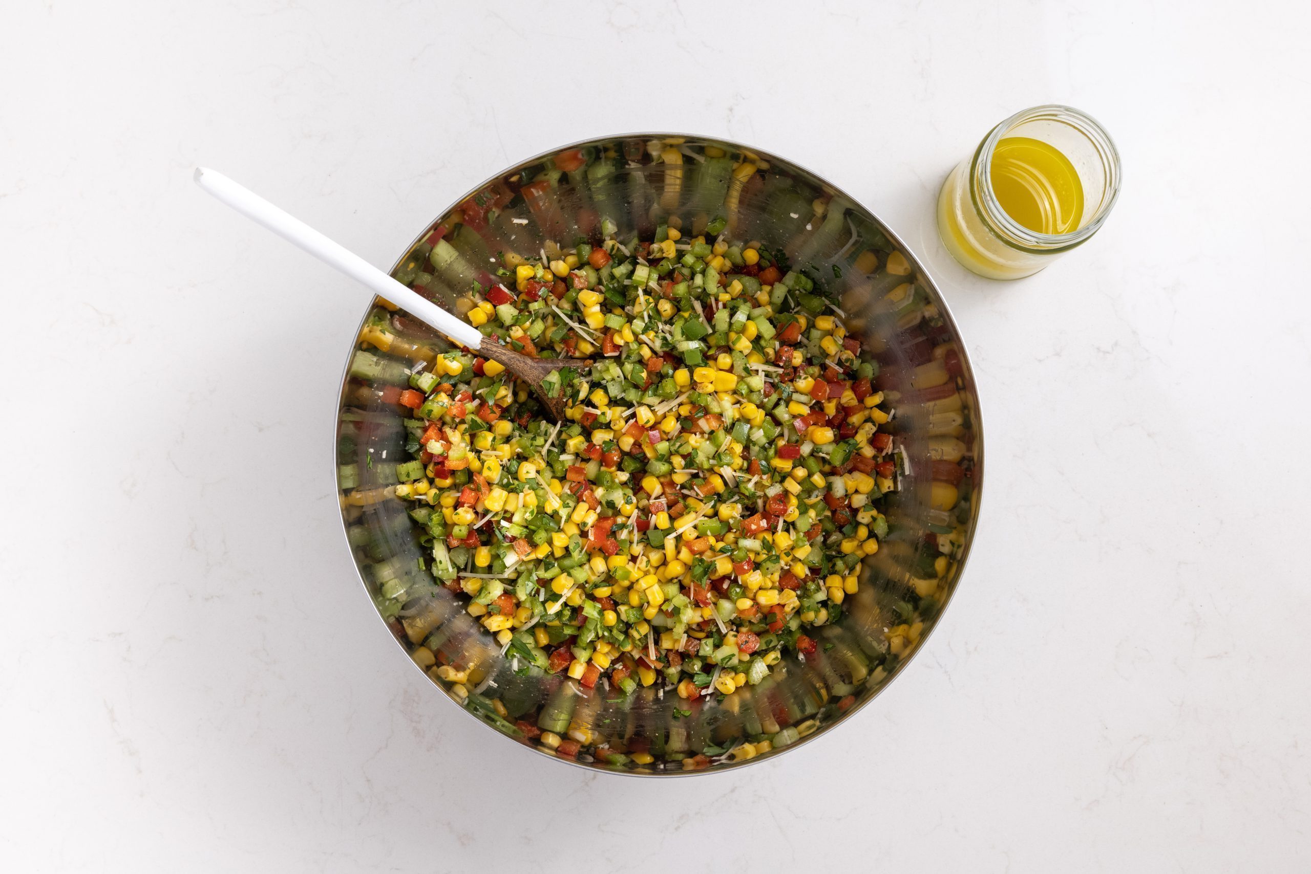 Ingredients for colorful corn salad mixed in large bowl with wooden spoon.