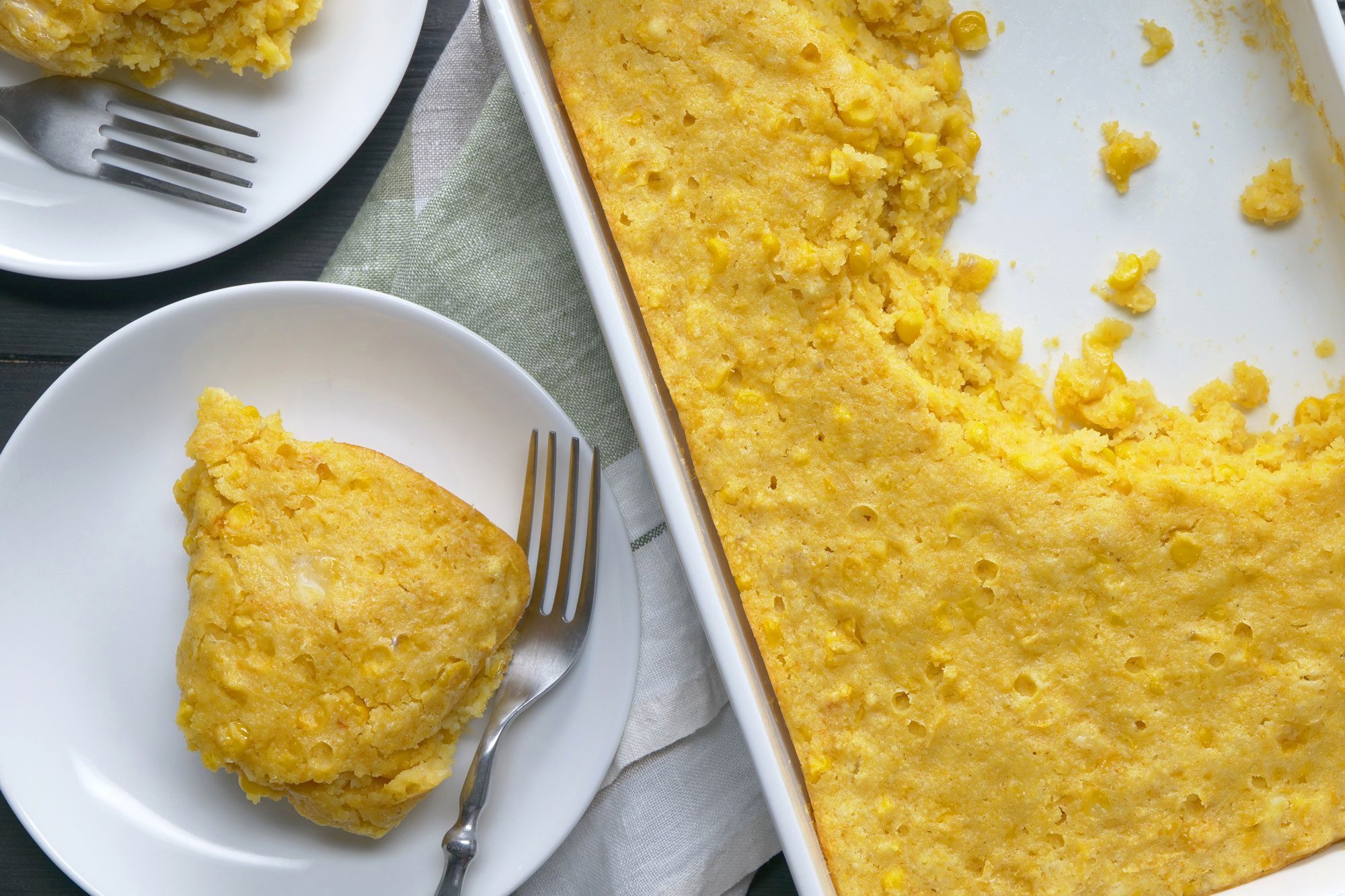 Cornbread Casserole served in two small white plates with silver forks placed over kitchen napkin