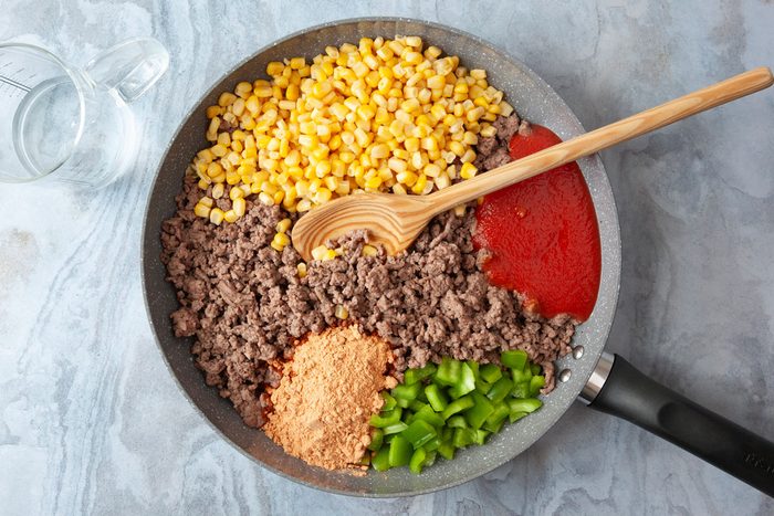 Step 1 of Taste of Home Cornbread Taco Bake is to cook the beef and drain it before adding the corn, pepper, taco seasoning and tomato sauce