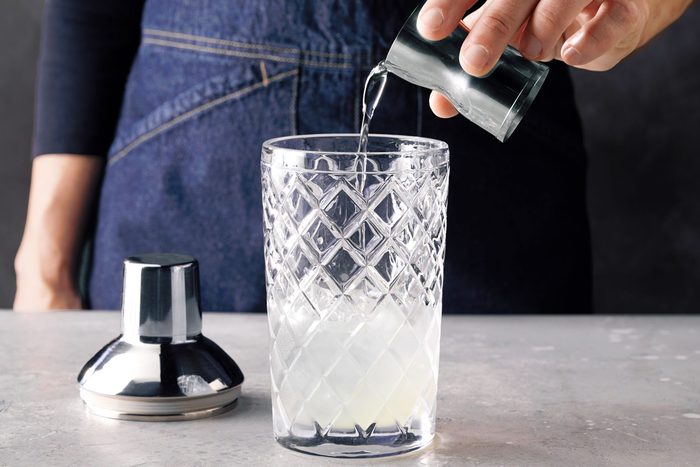 Table view shot of fill a shaker half full with ice; add gin; lemon juice and syrup; marble background;