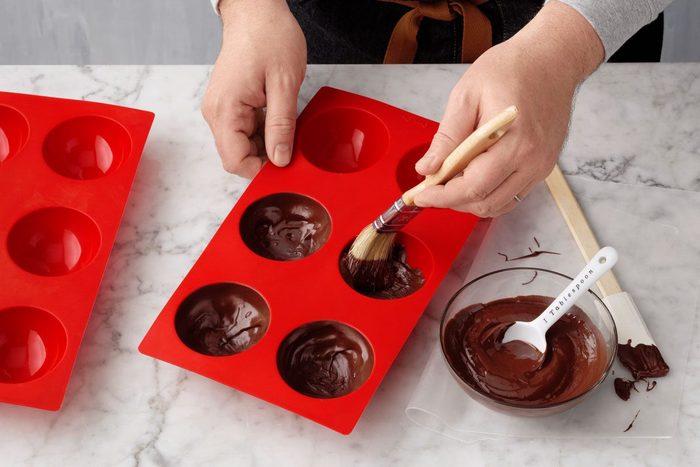 putting melted chocolate into a mold to make Hot Chocolate Bombs