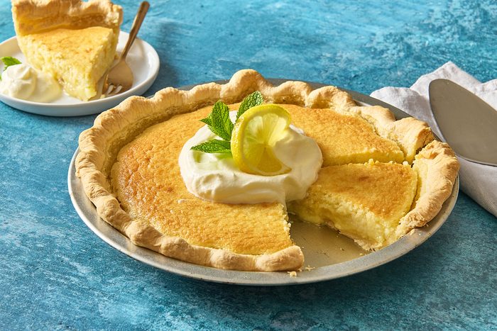 Lemon custard pie topped with whipped cream, lemon and mint