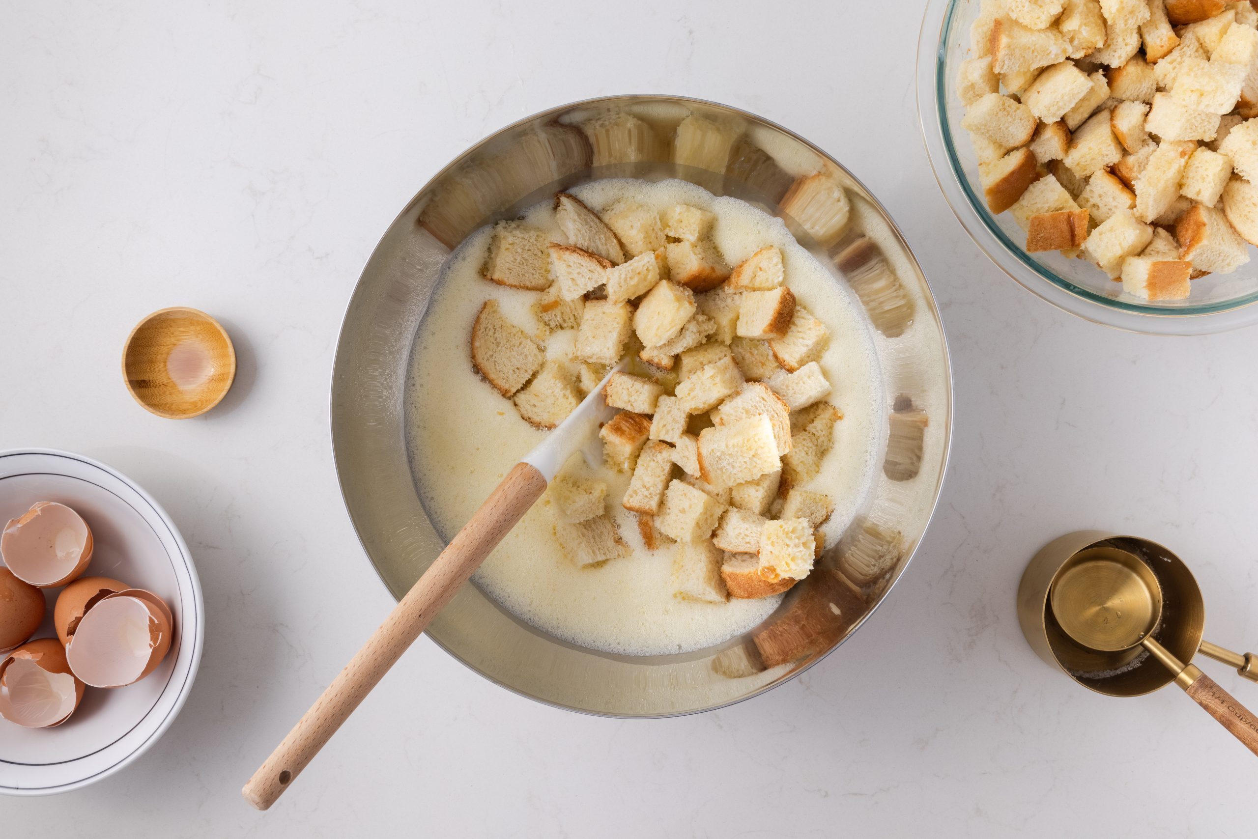 Bread being folded into eggs, raisins, vanilla, sugar and pineapple mixture.