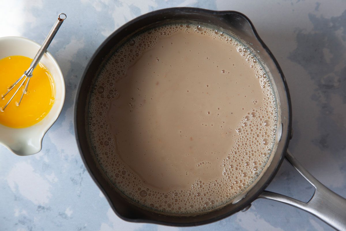 Egg yolk being tempered with warm milk mixture in heavy saucepan