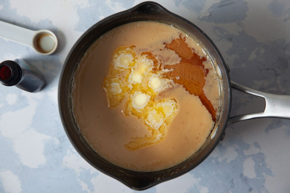 Butter and vanilla being added to milk pudding mixture in heavy saucepan.