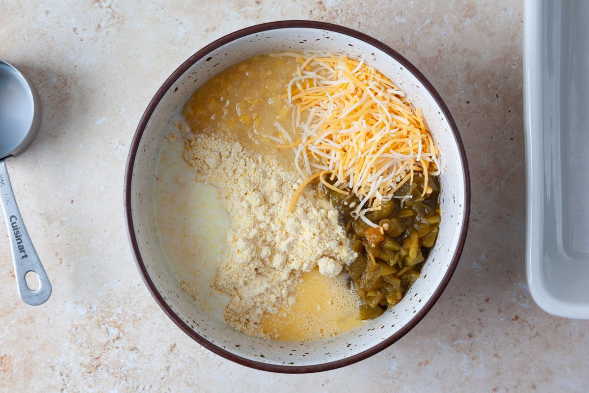Shredded cheese, cornbread mix, canned green chiles, milk, creamed corn and egg in a mixing bowl.