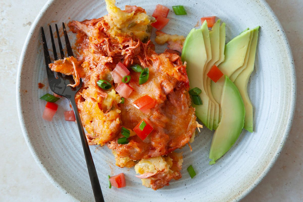 Single serving of chicken tamale casserole on a plate with avocado, tomatoes and green onions.