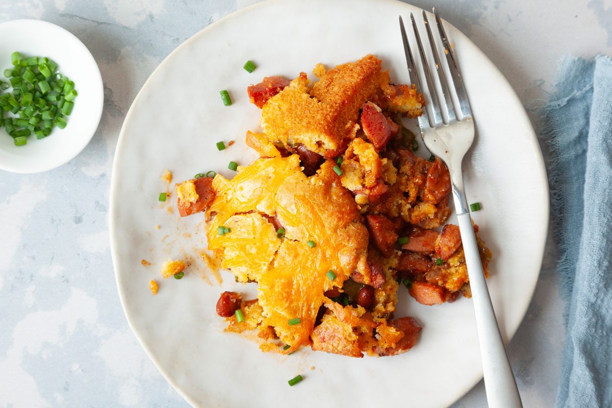 overhead angle of single serving of Taste of Home Chili Cheese Dog Casserole oh a white plate, garnished with chives