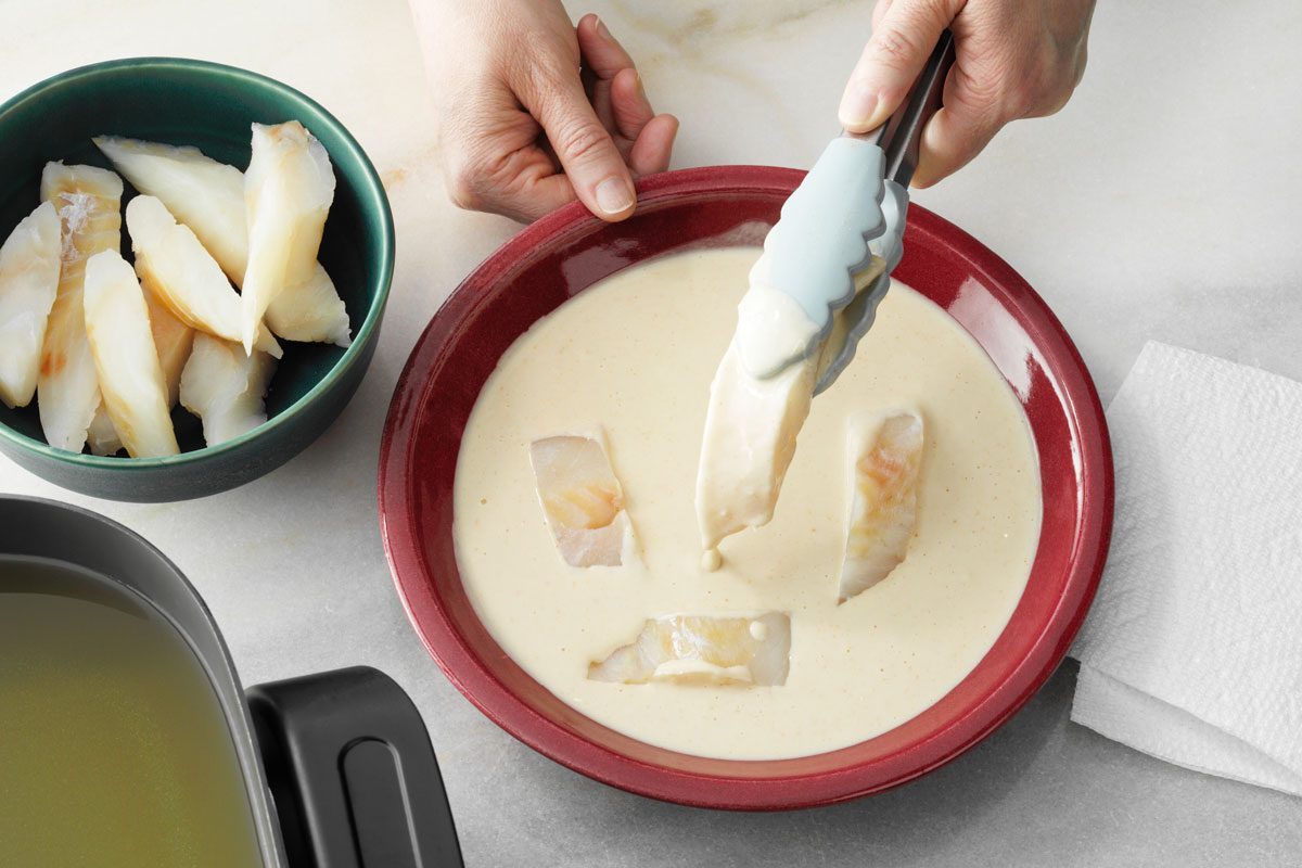 dipping fish in batter to make Beer Battered Fish Tacos