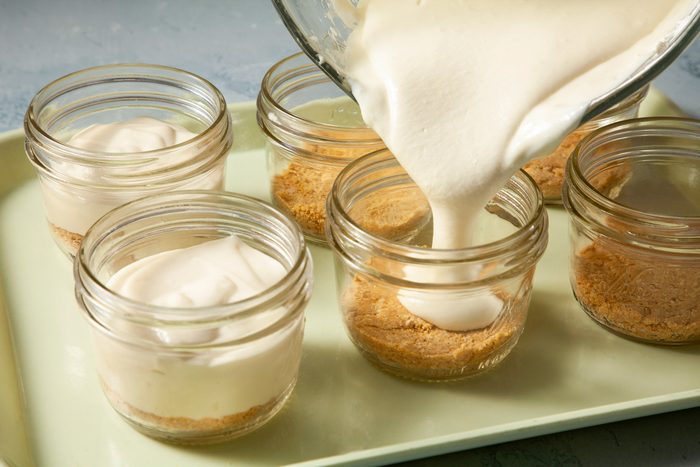 Cream cheese mixture being poured into glass jars.