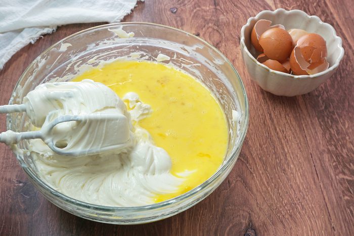 Beating eggs into a smooth cream cheese batter for amaretto cheesecake RMS 91184 for Taste of Home