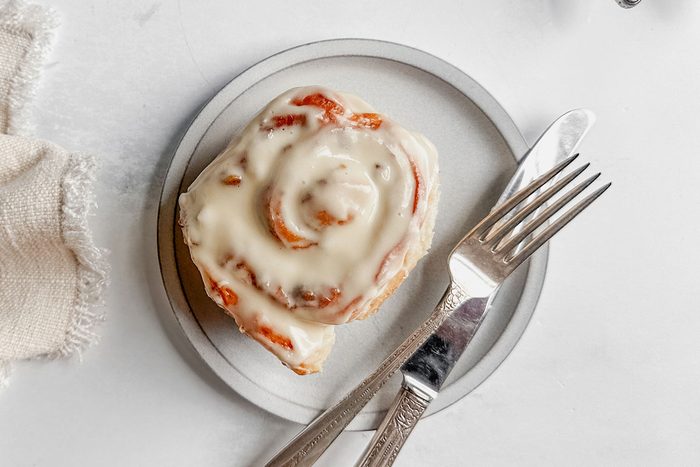 Taste of Home apple cinnamon roll on a white plate next to a cloth napkin on a marble surface.