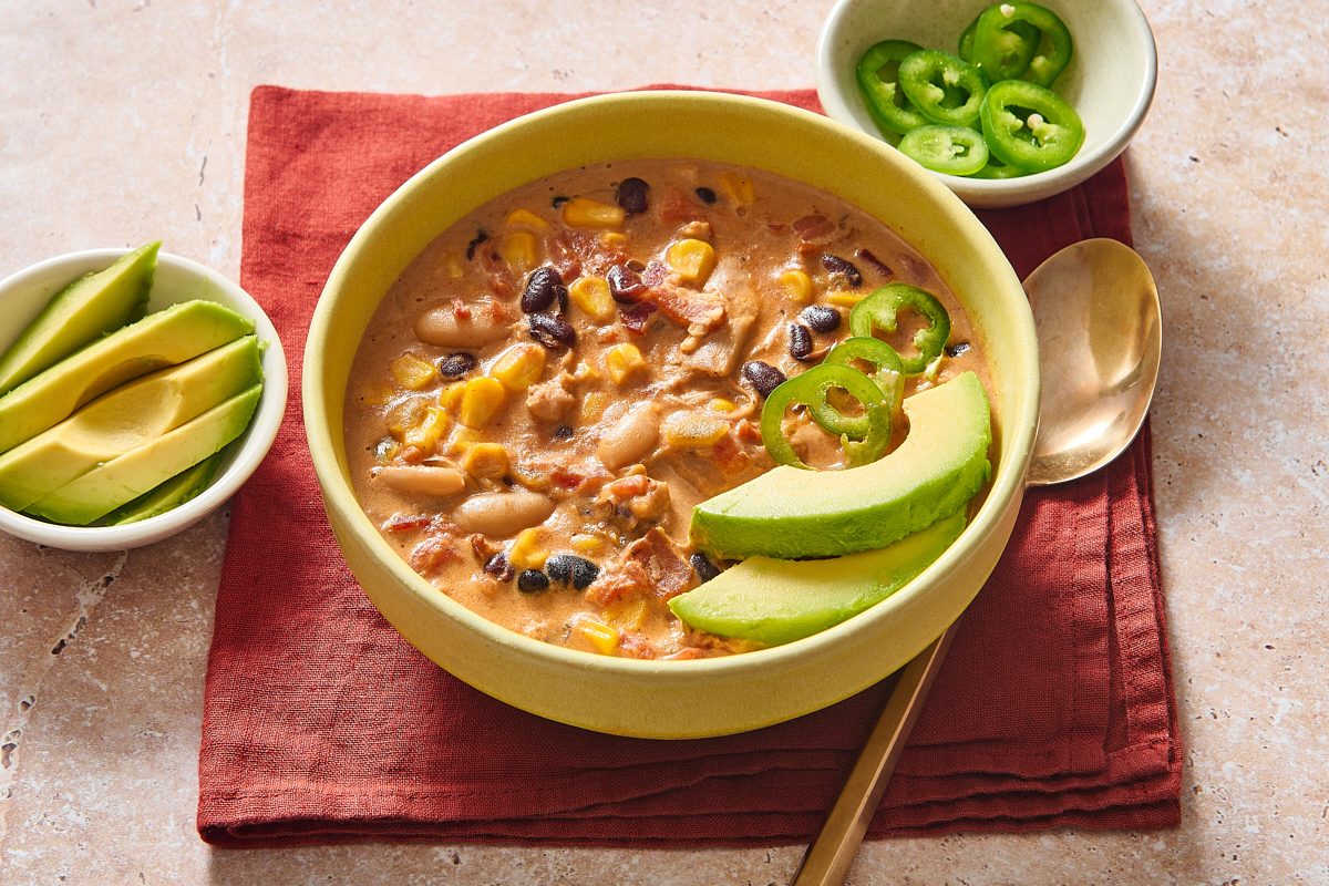 Shot of bacon chilli in a bowl topped with avocado and jalapeño