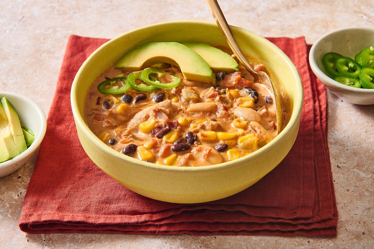Closeup of a bowl of bacon chilli with a spoon and added toppings
