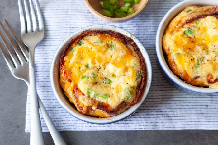 Taste of Home Bacon and Egg Muffins in blue ramekins, topped with green onions cheese, wooden bowl of green onions, forks