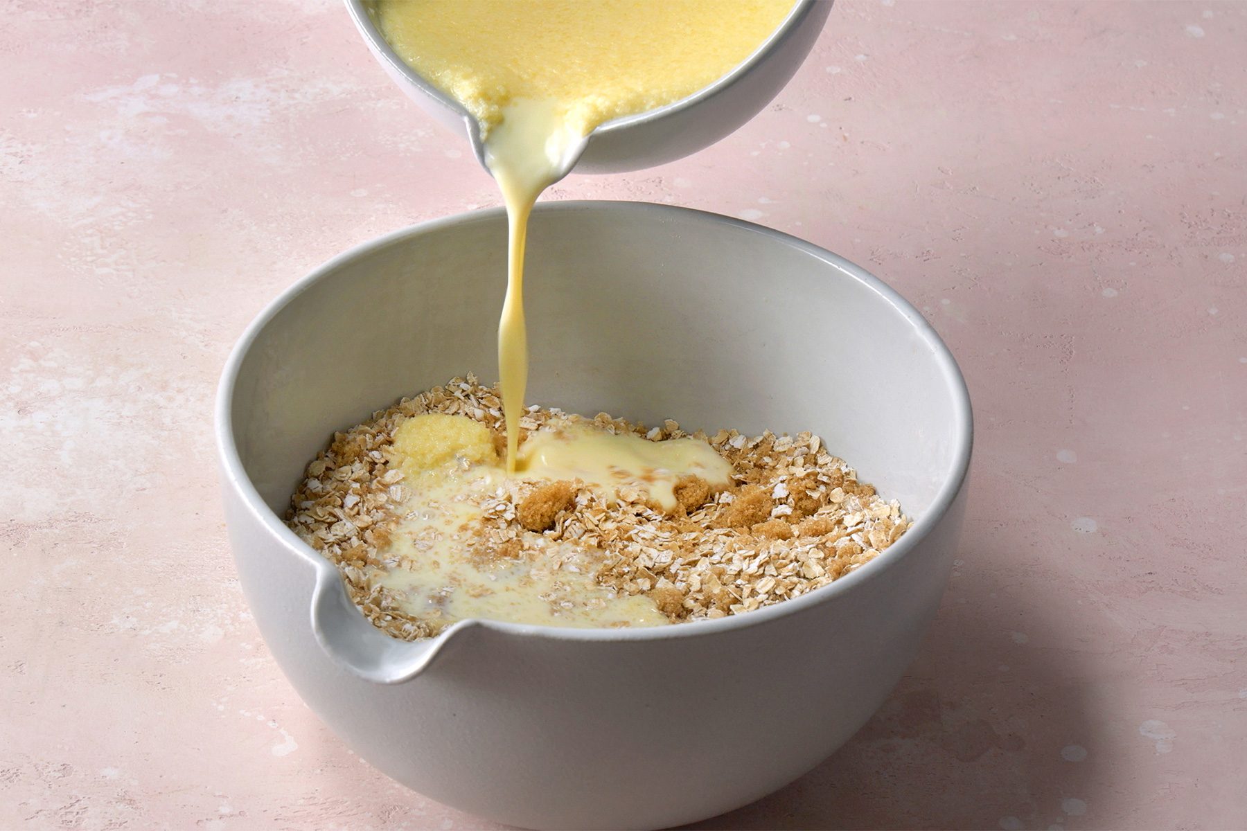 3/4th shot; light peach background; pouring whisk eggs, milk and butter mixture into the oats;