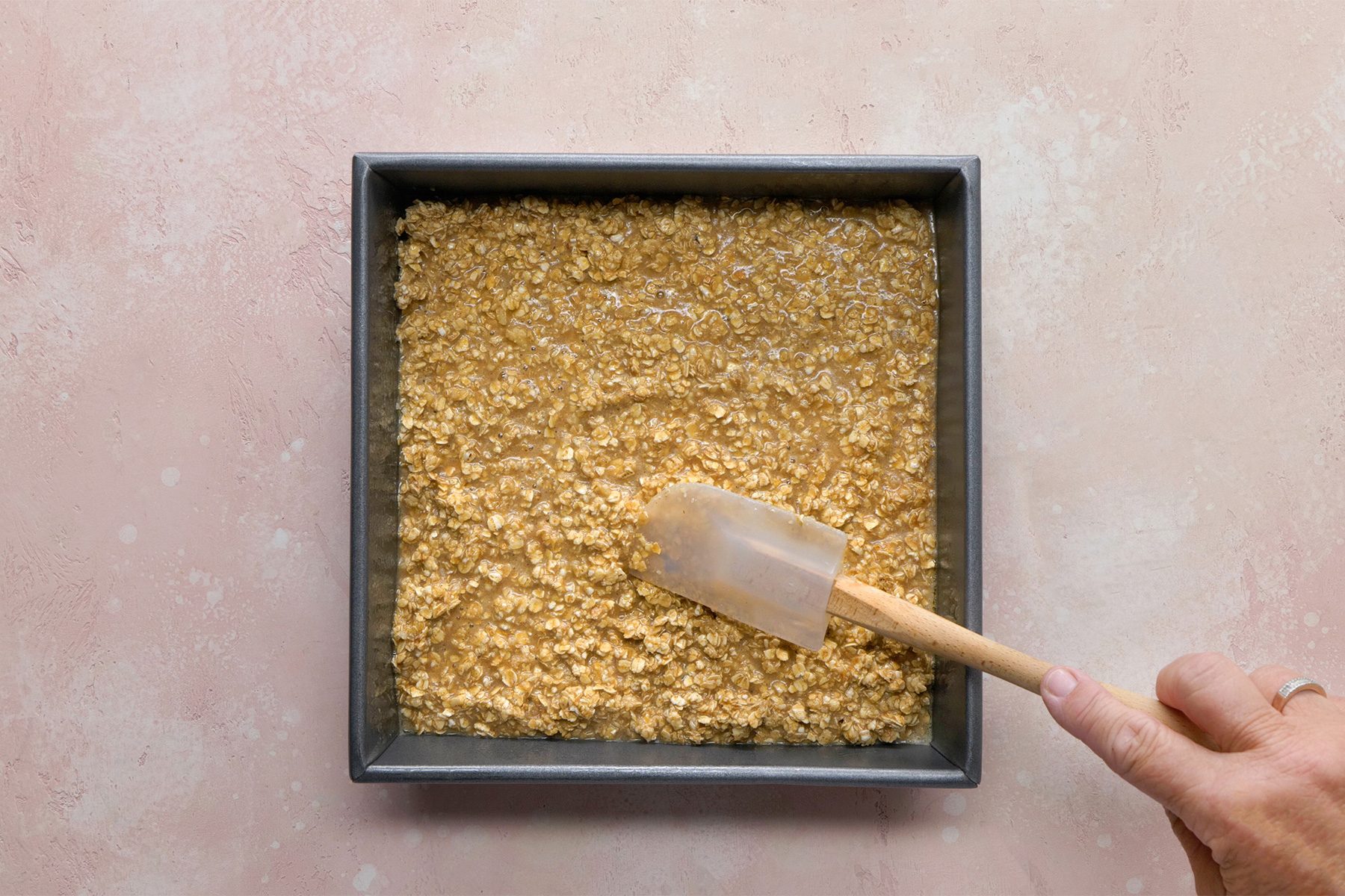 overhead shot; light peach background; Spooning into a greased square baking pan;