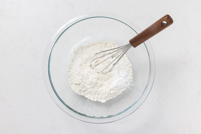 Flour, baking powder, baking soda and salt being mixed in bowl.