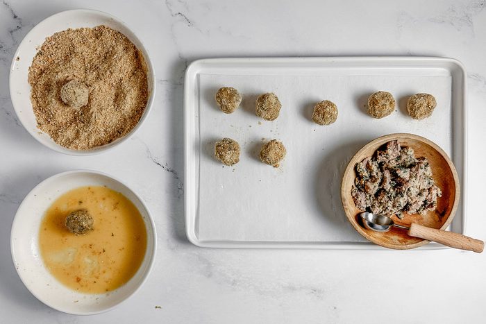 Taste of Home Bitterballen in bowls of bread crumbs and beaten egg next to breaded Bitterballen on a baking sheet.