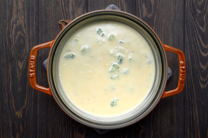 overhead shot; wooden background; Broccoli Cheddar Soup in a small saucepan;