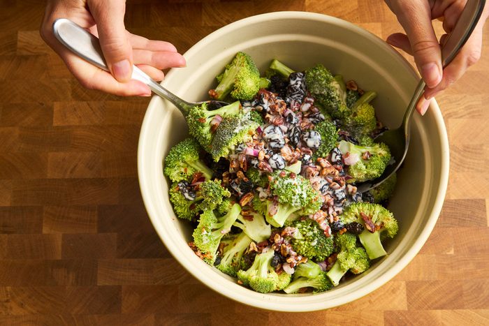 Bacon and broccoli salad in bowl being combined with dressing