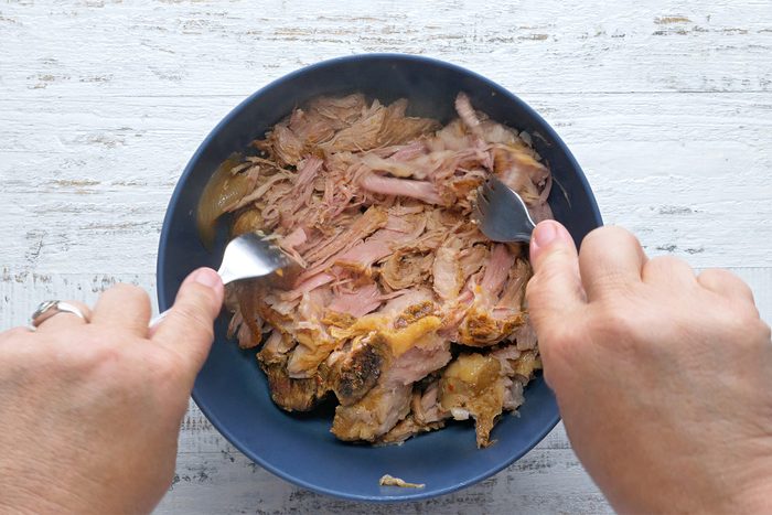 overhead shot; white textured background; Shredding pork with 2 forks in a bowl;