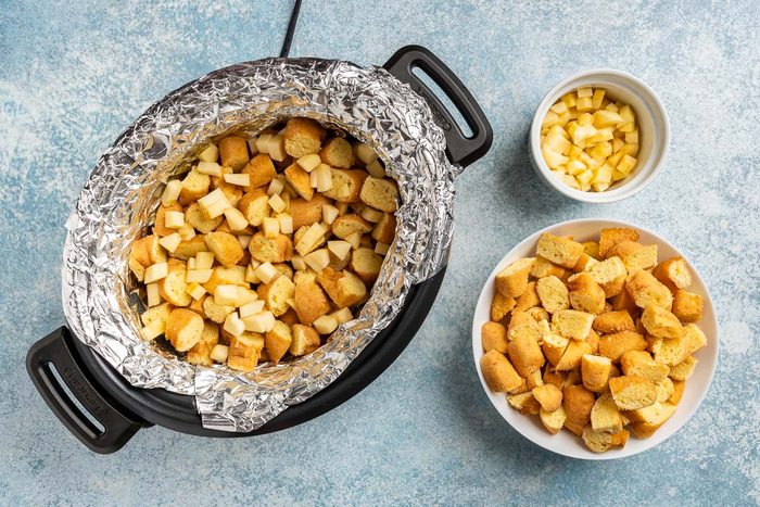Taste of Home Donut Bread Pudding recipe photo of layering the donuts and apples in the slow cooker.