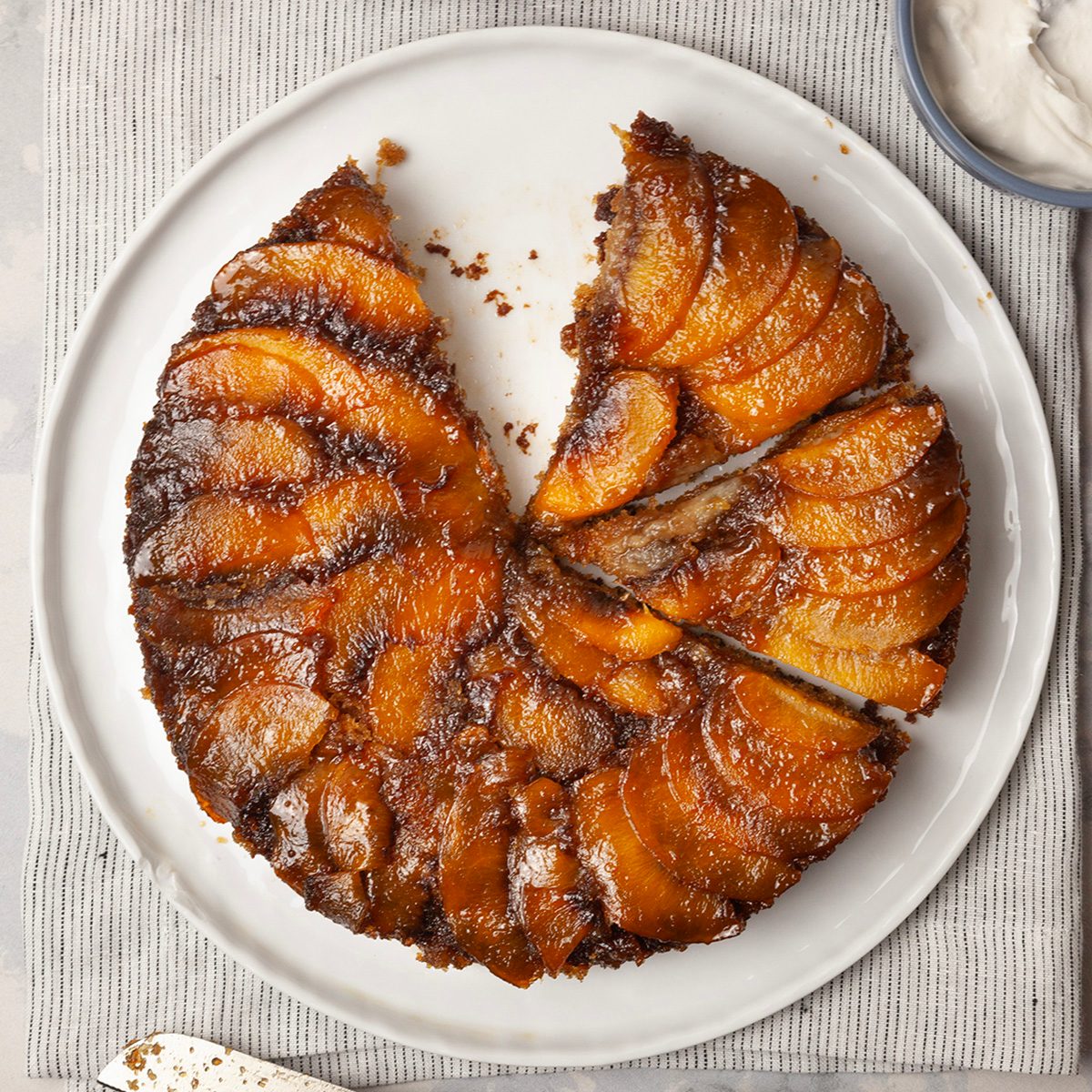 Full yield of Taste of Home Peach Upside-Down Cake on a white platter, blue bowl of whipped cream