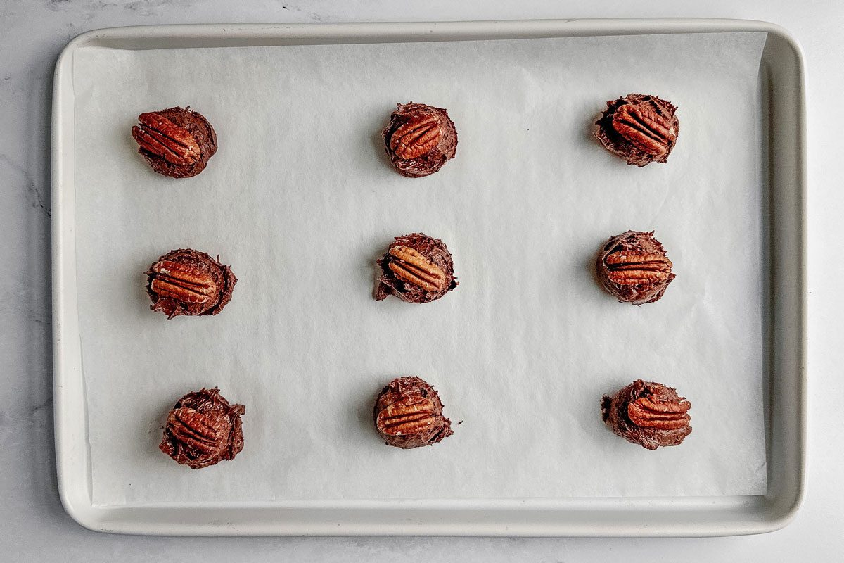 Unbaked Taste of Home German chocolate cookies on a white baking sheet on a marble surface.