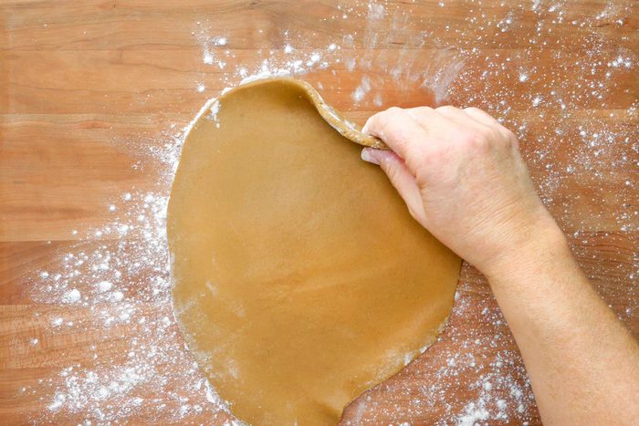 A hand lifting dough in the shape of a disk from a wooden surface.