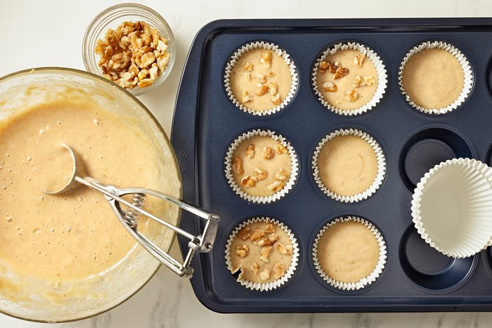 Muffin cups lined with paper are being filled with batter.