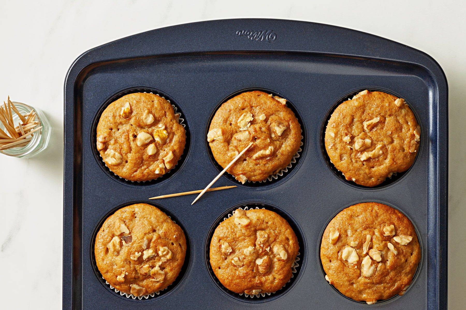 Muffin cups with baked muffins with toothpicks on them.