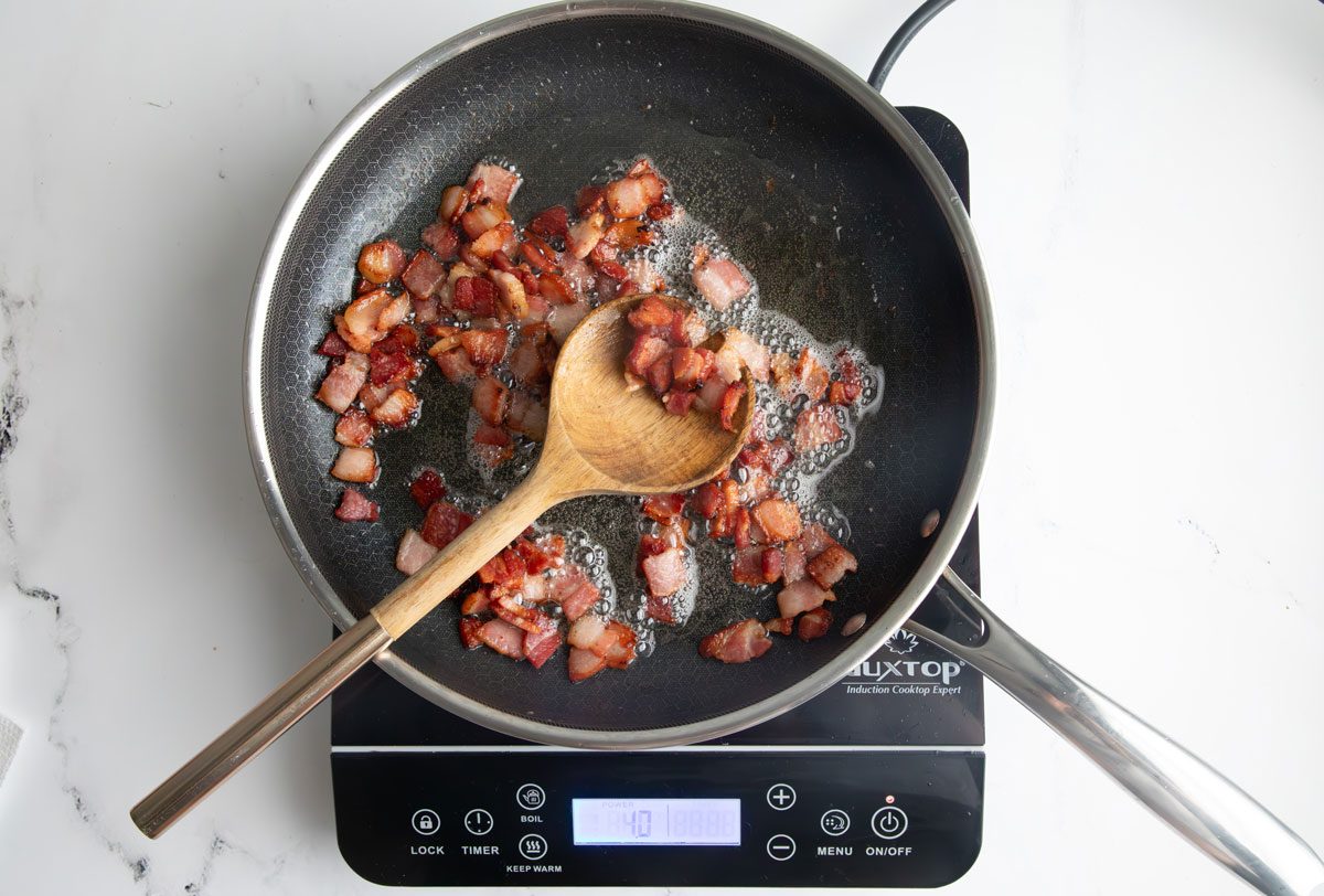 Finished bacon for Taste of home green beans and potatoes in a portable induction cooktop on a marble surface.