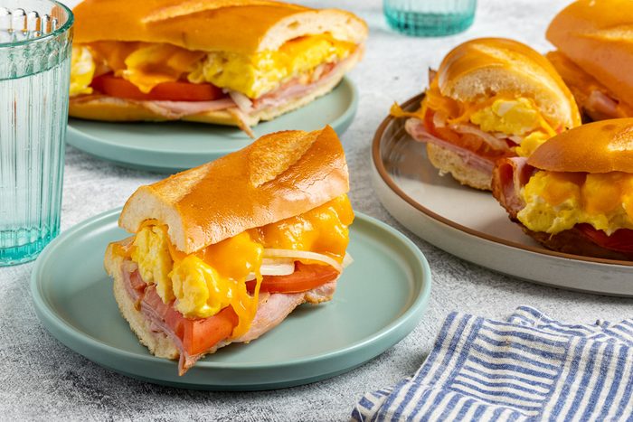 Taste of Home Ham Egg and Cheese Sandwich recipe photo of the sandwich cut into slices and set on a serving platter and plates.